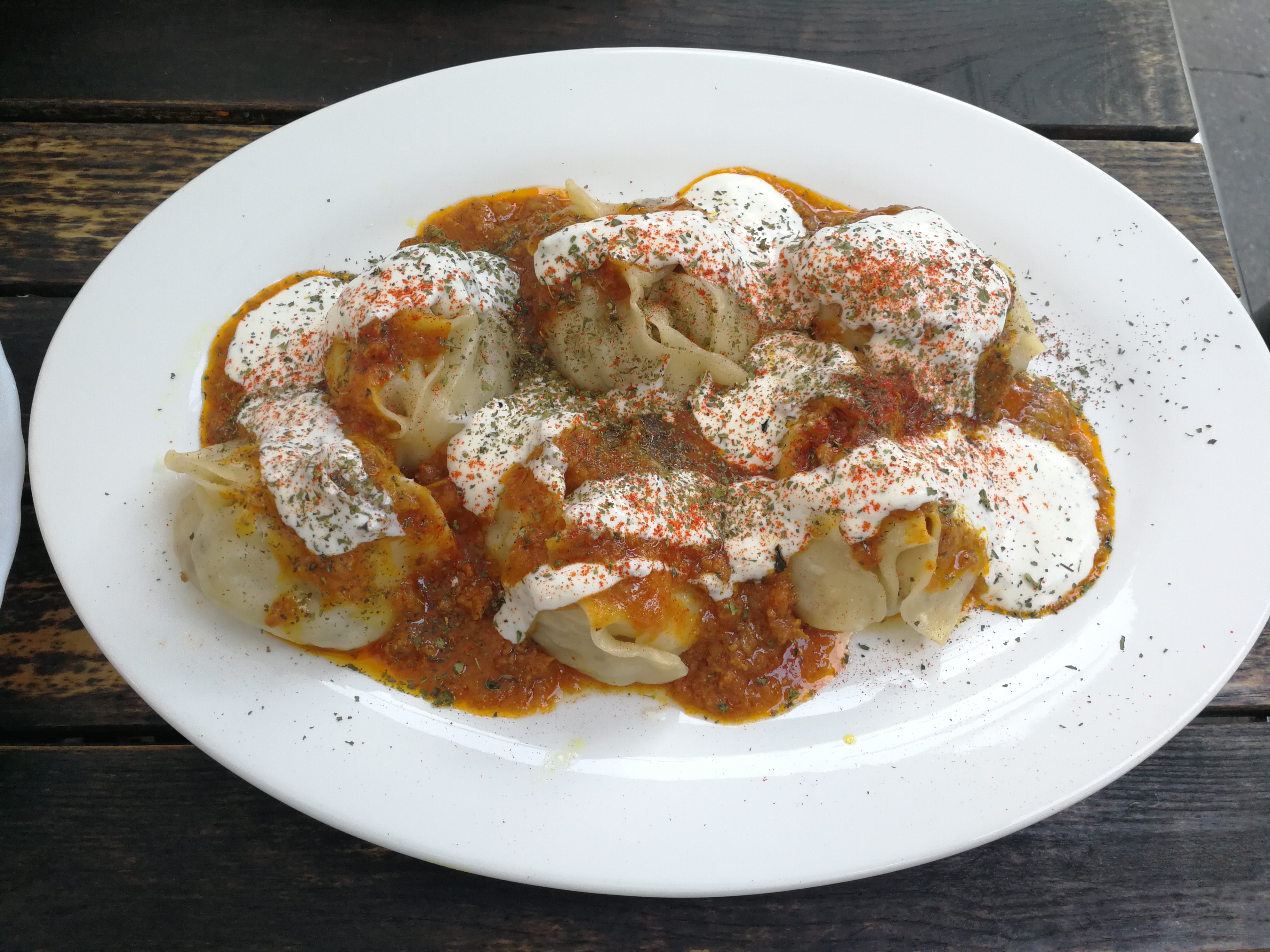 A plate of Afghan mantu: steamed dumplings filled with minced meat and onion, topped with garlic yogurt and a split-pea garnish