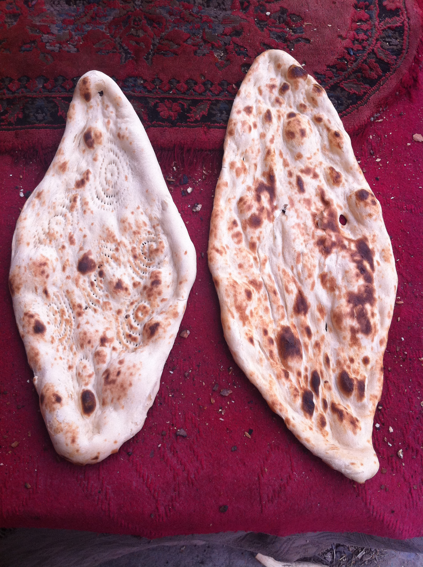 Stretched and dimpled rounds of dough alongside finished tandoor-baked Afghan flatbread, photographed in Nangarhar, Afghanistan